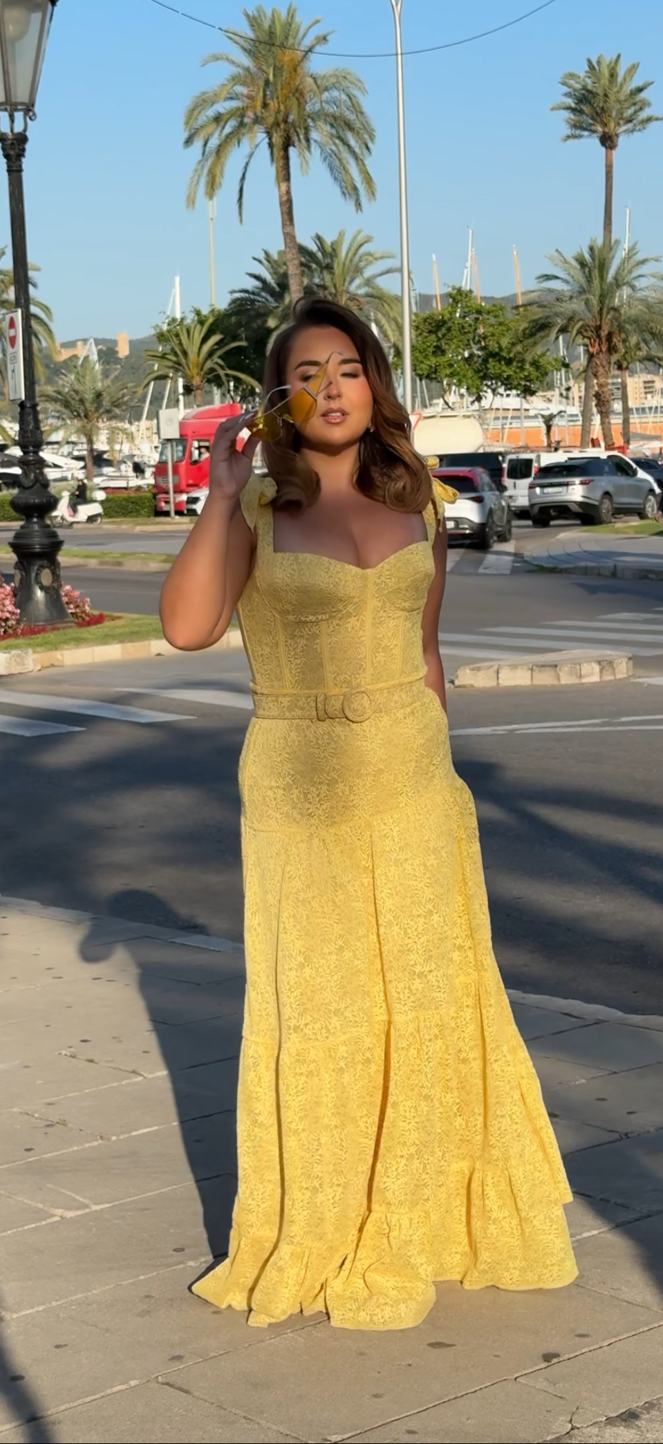 Woman in a yellow dress standing on a street with palm trees in the background